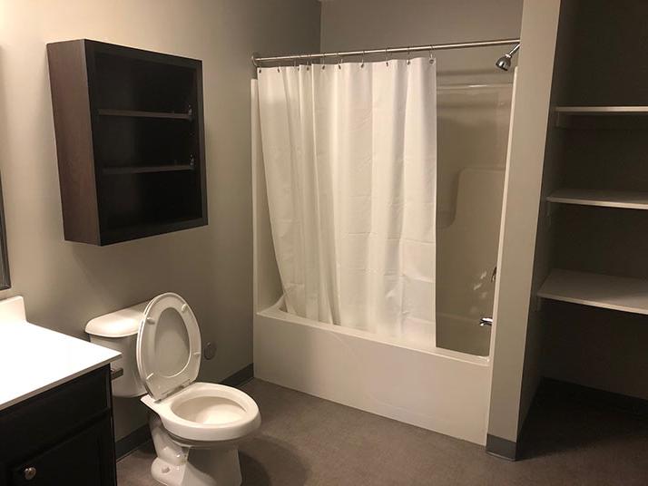 bathroom with shower, toilet, a cabinet, and shelves